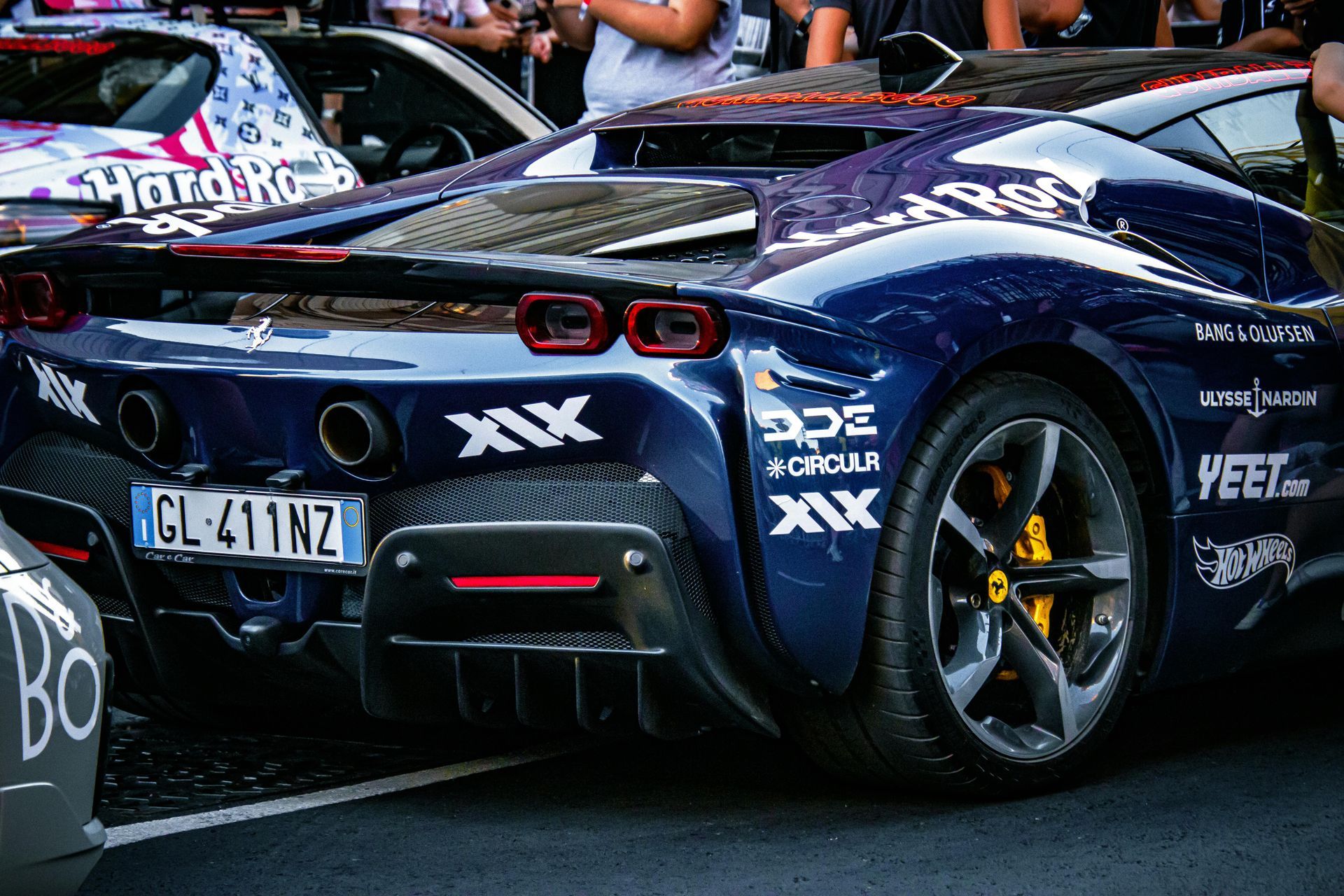 Blue Ferrari sports car with sponsor logos, parked at an event.