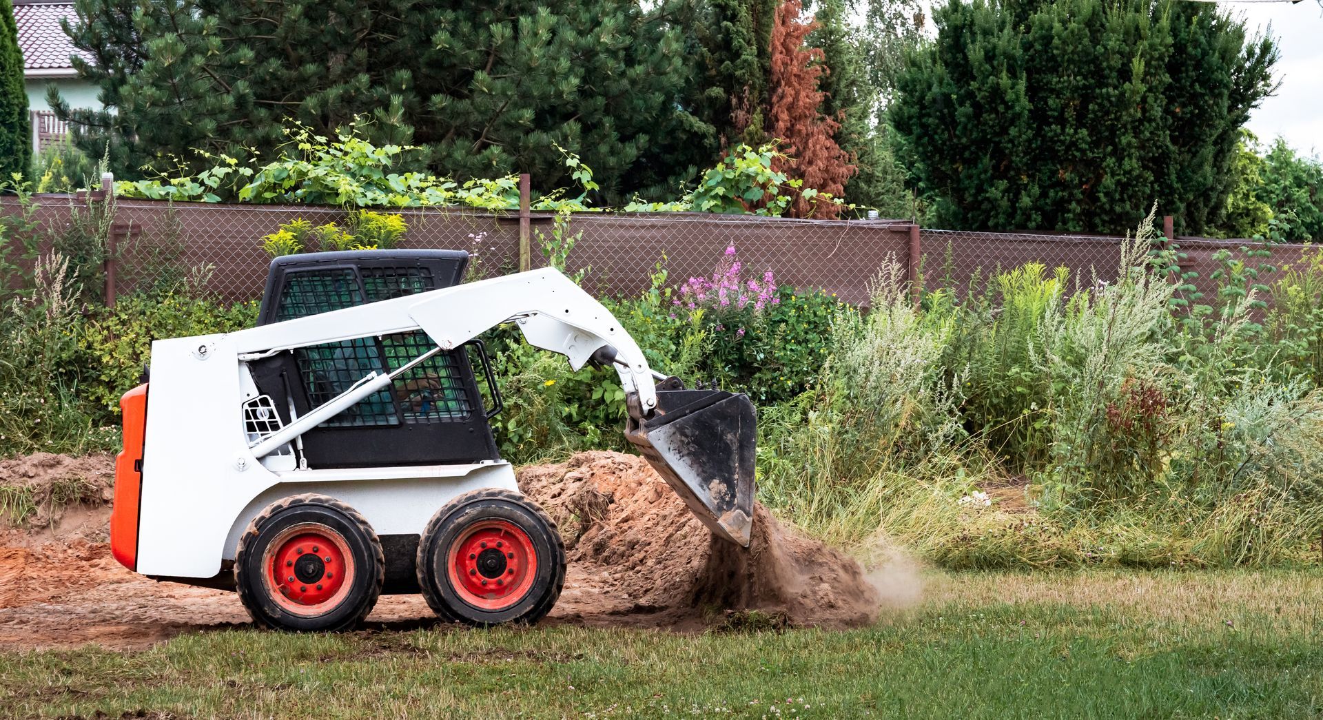 White skid-steer loader pushing a dirt pile on a grassy field, with dust and shrubs in the background
