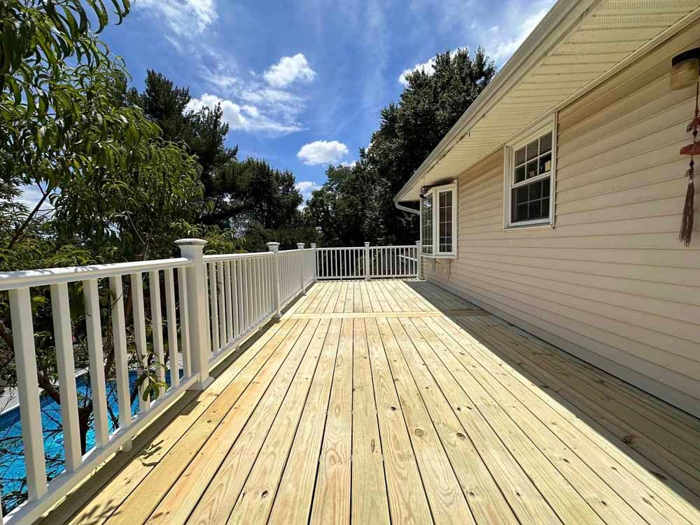 Wooden deck with white railing next to a house under a blue sky.