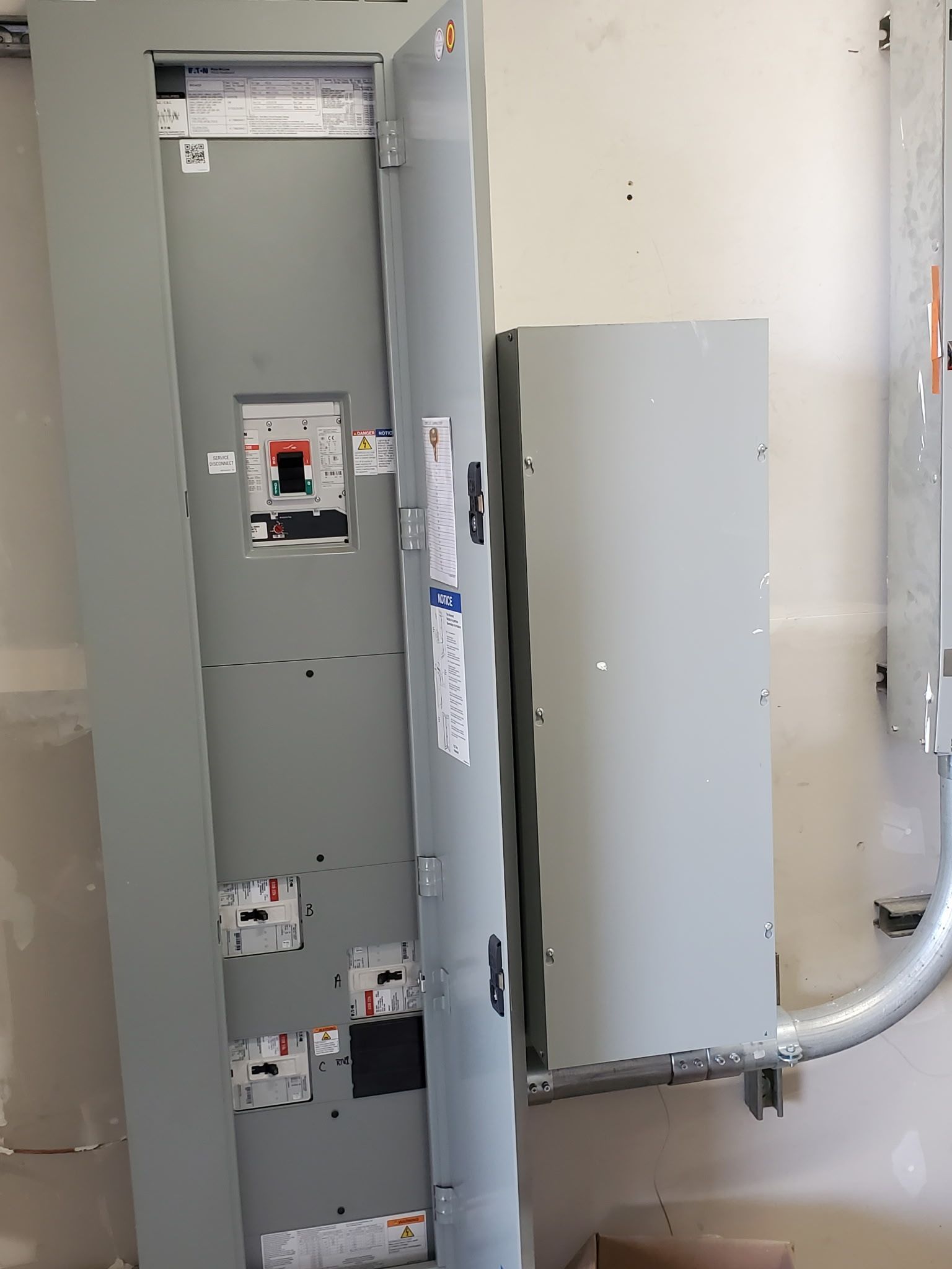 Large gray electrical panel with a smaller gray box attached to a wall.