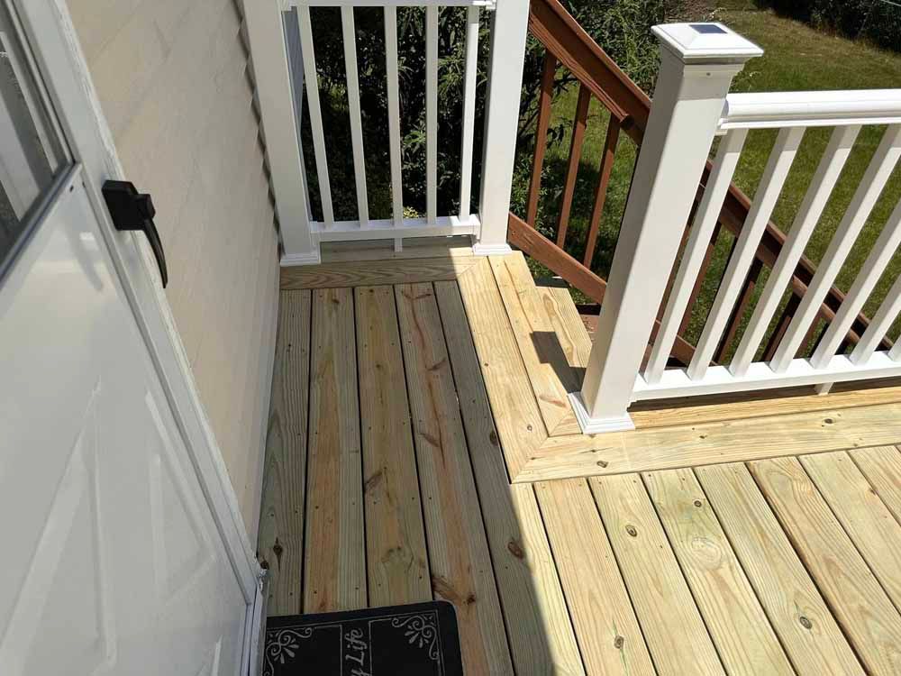 Wooden deck with white railing and stairs next to a white door.