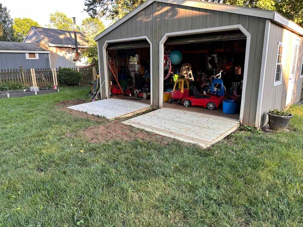 A two-car garage with open doors. Cement pads are in front. Yard with green grass and garden is visible.