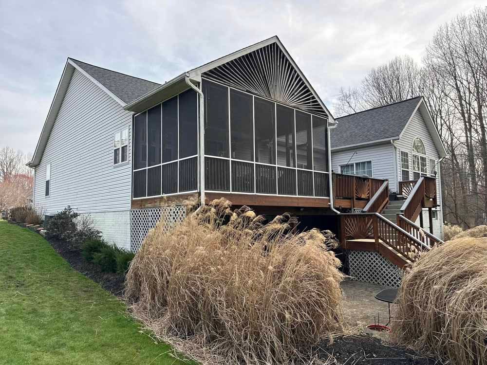 House exterior with screened porch, wooden deck, and landscaping on a grassy hill.