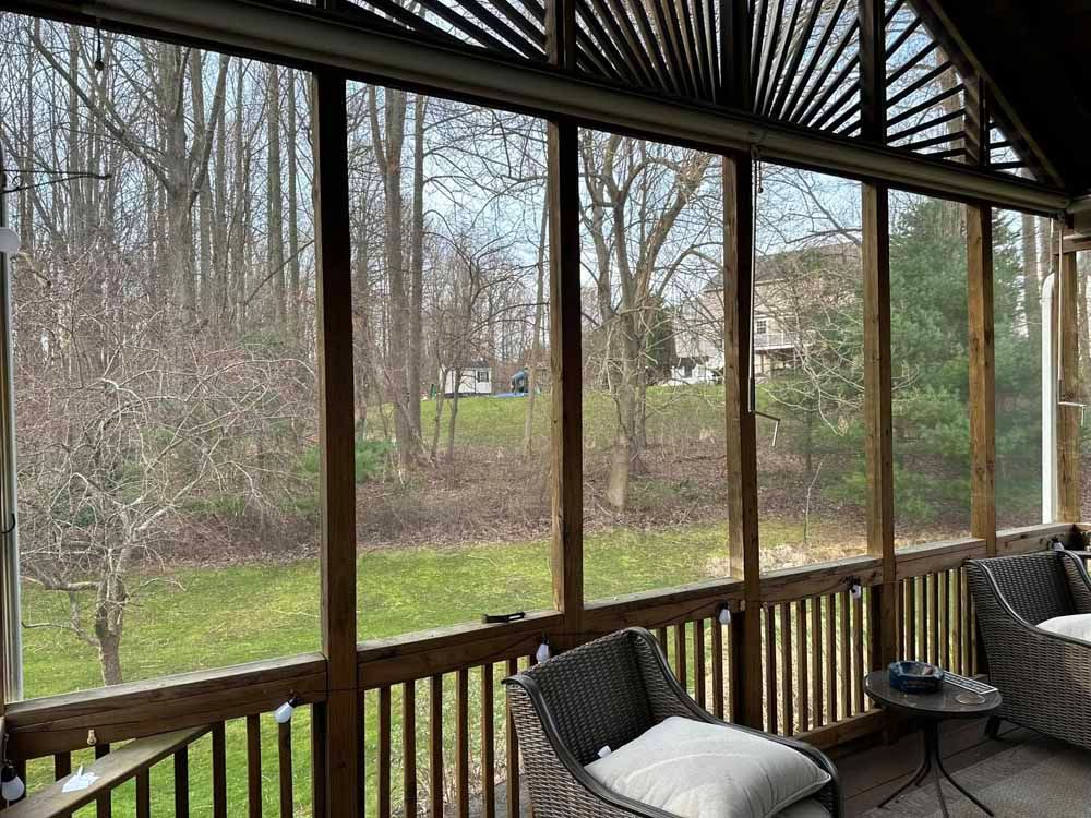 Screened porch with wooden railings and chairs overlooking a yard and trees.