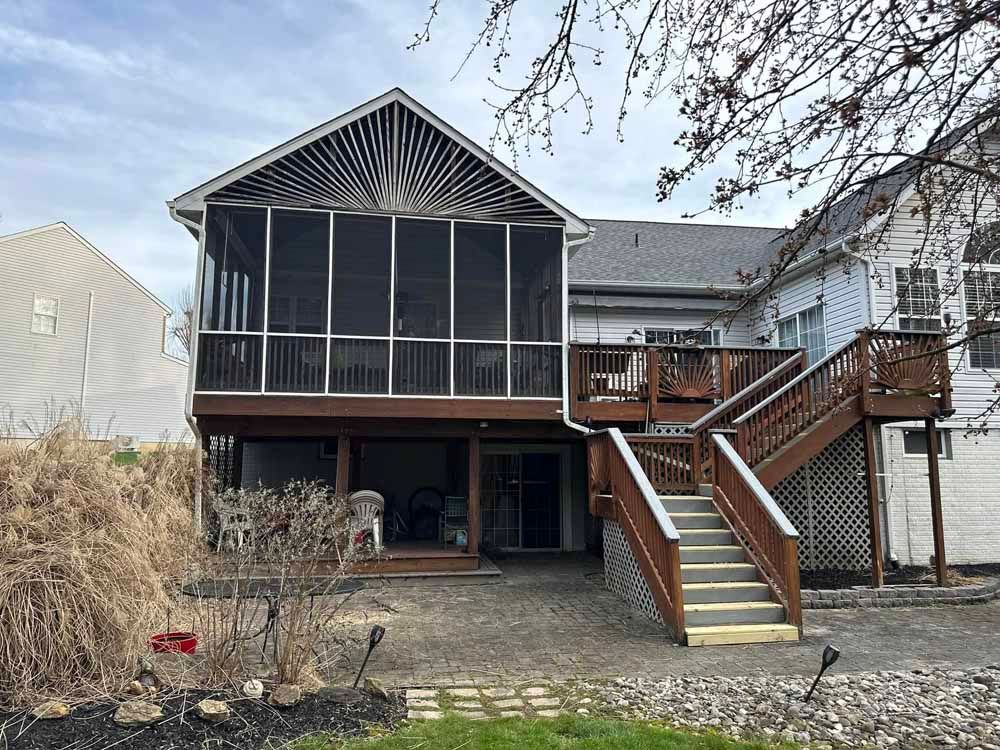 Back of a two-story house with a screened porch and wooden deck; gray siding, brown deck and stairs.