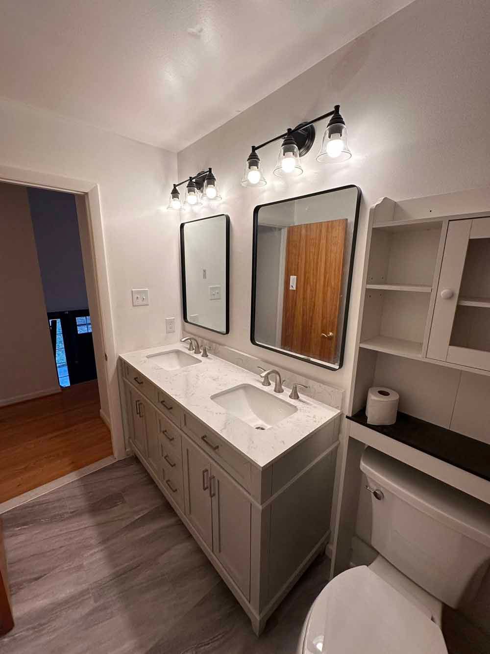 Bathroom with a white double vanity, mirrors, and a toilet. Gray wood-look floor.