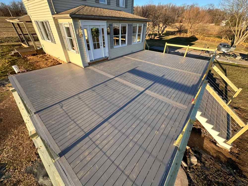 Newly constructed deck with gray composite decking, attached to a light-colored house with a porch and steps.