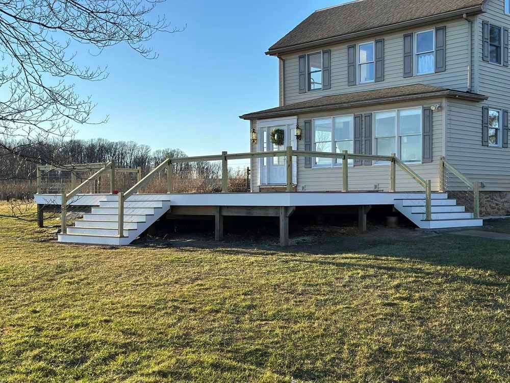 A two-story house with a wooden deck and staircase. The deck is painted white with a wooden railing.