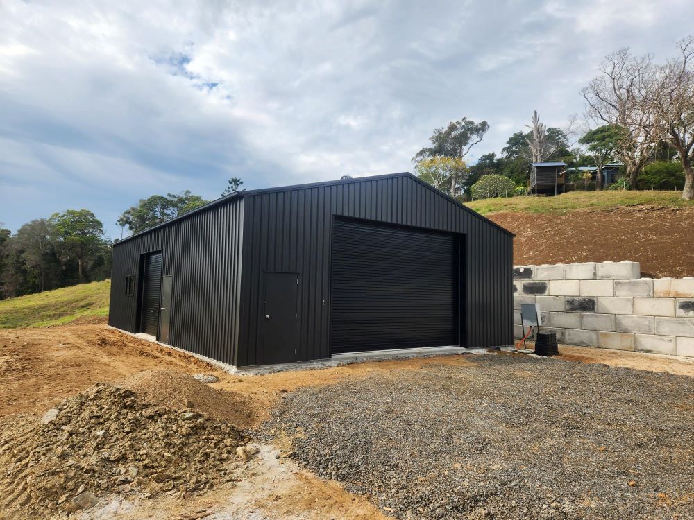 A Black Garage With A Garage Door Is Sitting On Top Of A Dirt Hill — Whit Coast Sheds in Moranbah, QLD
