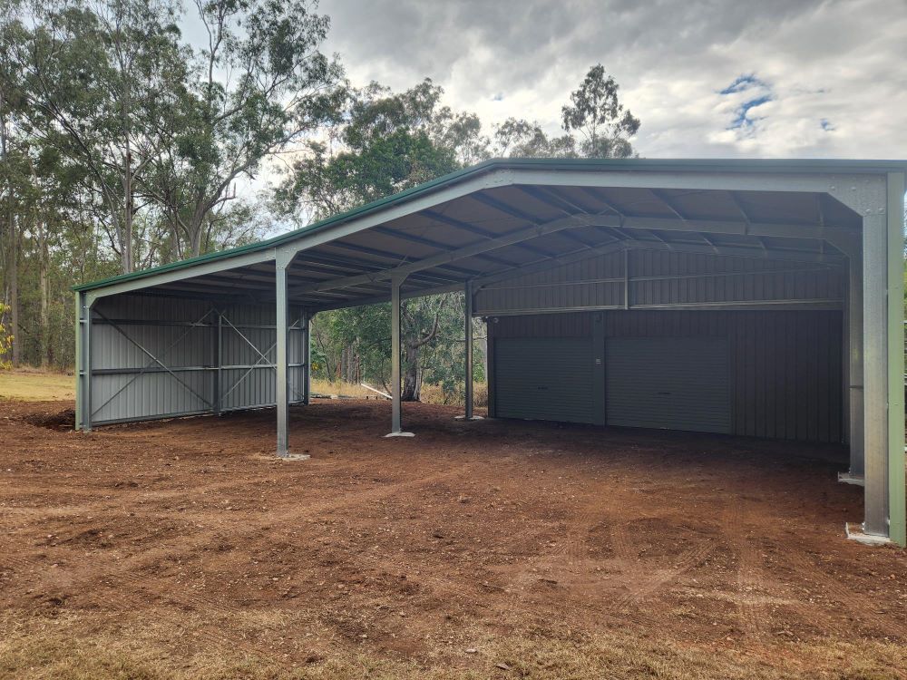 A Large Metal Building With A Green Roof Is Sitting In The Middle Of A Dirt Field — Whit Coast Sheds in Gregory River, QLD