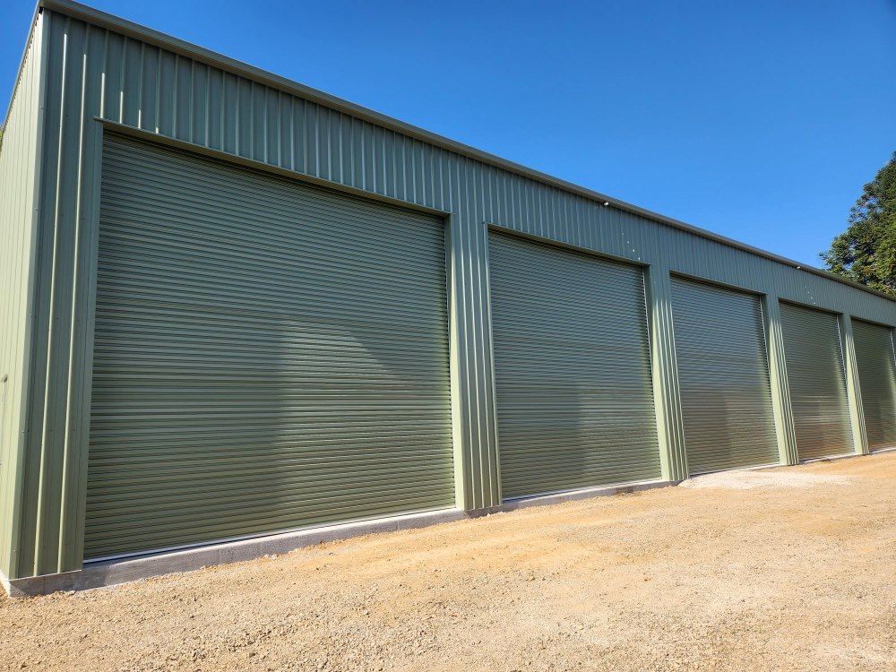 A Row Of Green Garage Doors With A Blue Sky In The Background — Whit Coast Sheds in Bowen, QLD