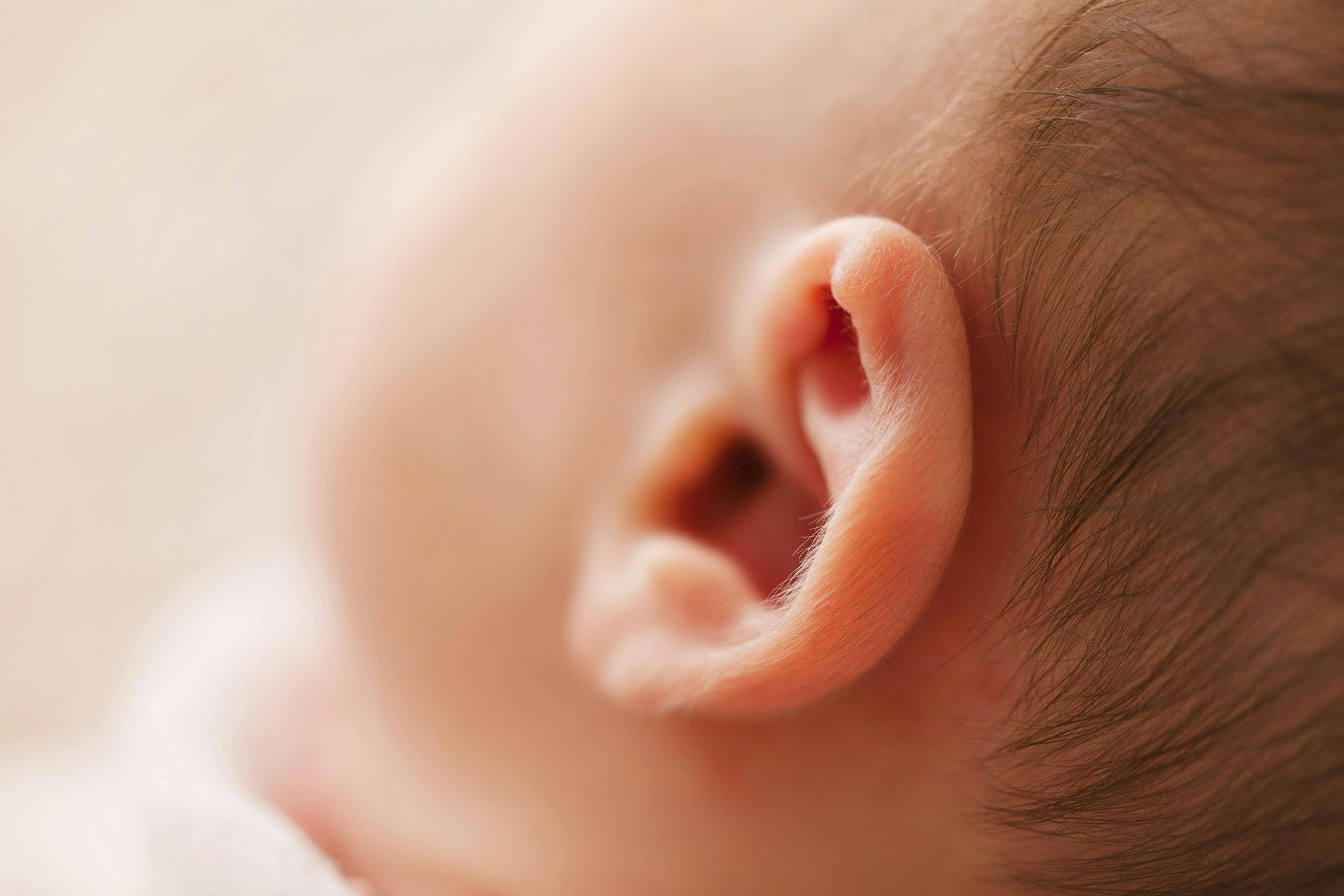 Close-up of a baby's ear, light skin, soft curls, shallow focus.