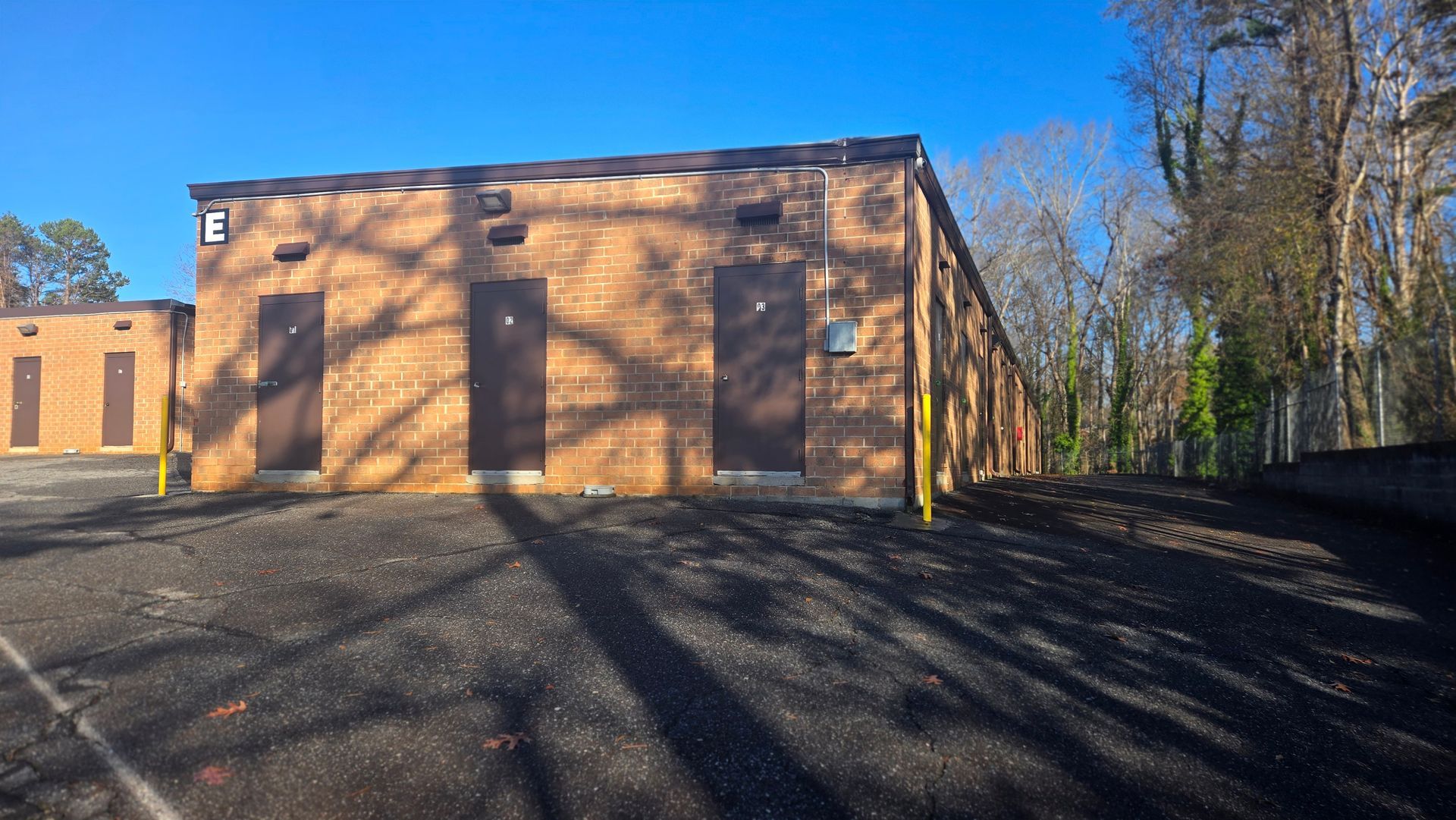 A brick building with a parking lot in front of it and trees in the background.