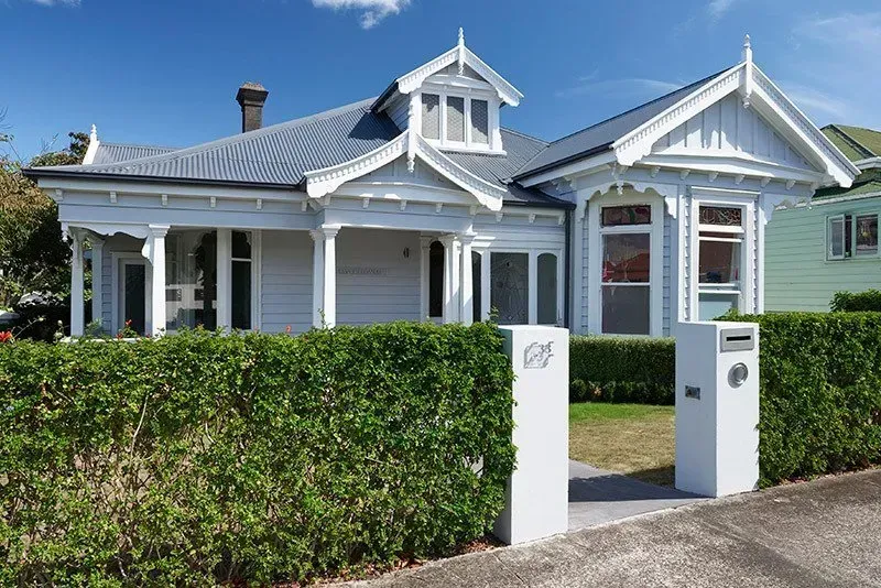 A White House with a Gray Roof is Surrounded by a Green Hedge — Auckland, NZ — Pro Roofing