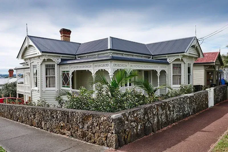 A White House with a Black Roof is Surrounded by a Stone Wall — Auckland, NZ — Pro Roofing