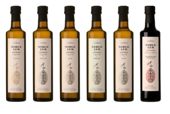 Seis botellas de aceite de oliva, de vidrio ámbar, con tapón negro y etiqueta blanca con la inscripción 