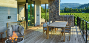 Outdoor deck overlooking a vineyard, with a table and chairs, a fireplace, and a glass door.