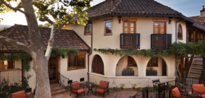 Exterior of a two-story building with a brown tiled roof. Beige stucco walls, arched openings, and small balconies are visible.