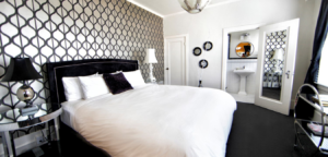 Bedroom with black and white patterned wallpaper, bed, and vanity area.