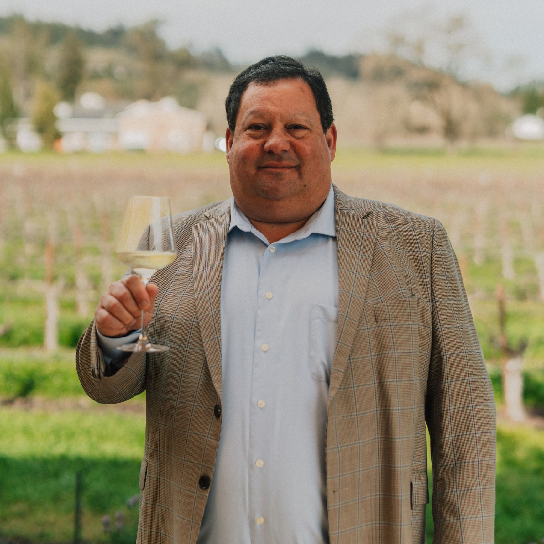 Man wearing blazer, smiling outdoors.