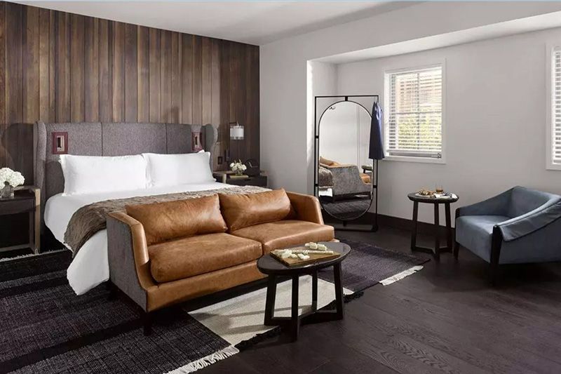 Hotel room with a bed, brown leather sofa, and dark wood paneling on the wall.