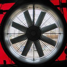 Großer, geschlossener Industrieventilator mit acht Flügeln, Metallgitter, roter Hintergrund.