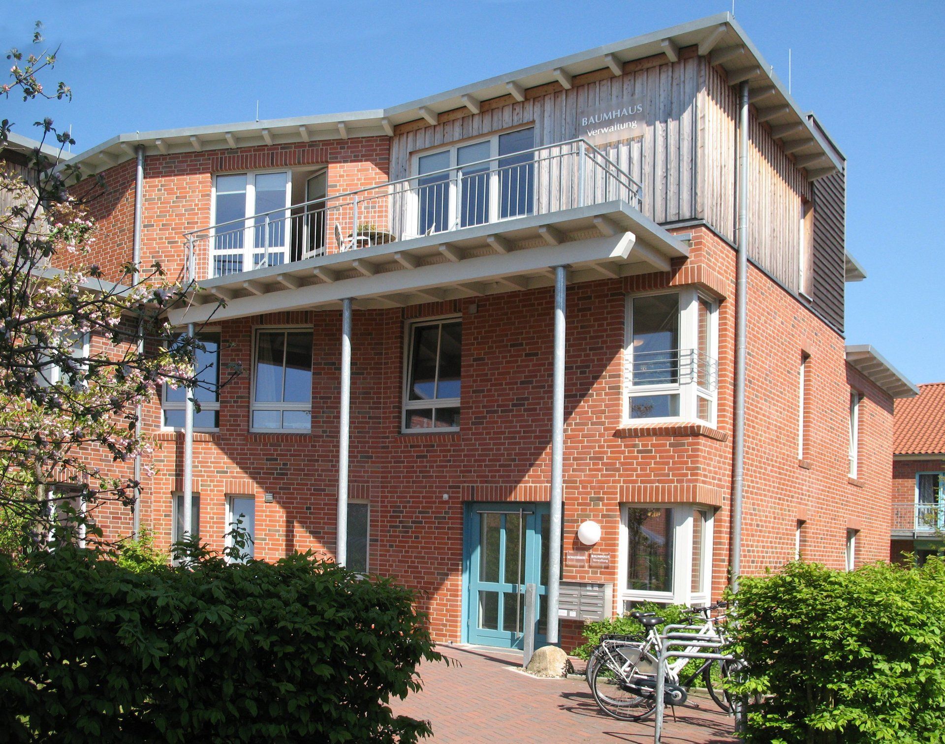 Ein rotes Backsteingebäude mit blauer Tür, weißen Zierelementen und einem Balkon an einem sonnigen Tag.
