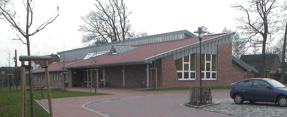 Backsteingebäude mit rotem Dach, schrägen Fenstern und einem davor geparkten blauen Auto.