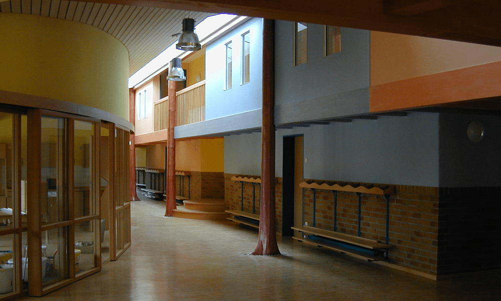 Flur mit farbenfrohen Wänden, Holzsäulen und Bänken. Balkon im Obergeschoss.