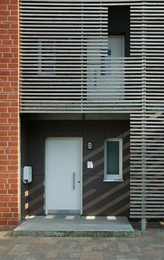 Moderne Gebäudefassade mit weißer Tür, Holzlatten, Backsteinmauer und kleinem Fenster.