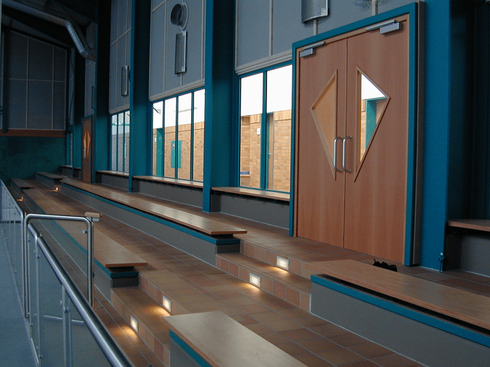 Interieur mit Holztüren, eingebauten Sitzbänken und Fenstern. Türkisfarbene Wände, Holz- und Grautöne.