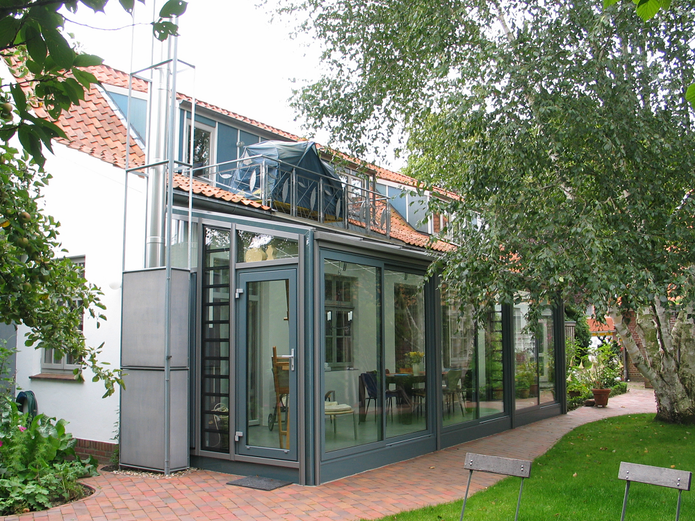 Verglaster Gebäudeanbau mit Solarpaneelen und einem Ziegelweg.