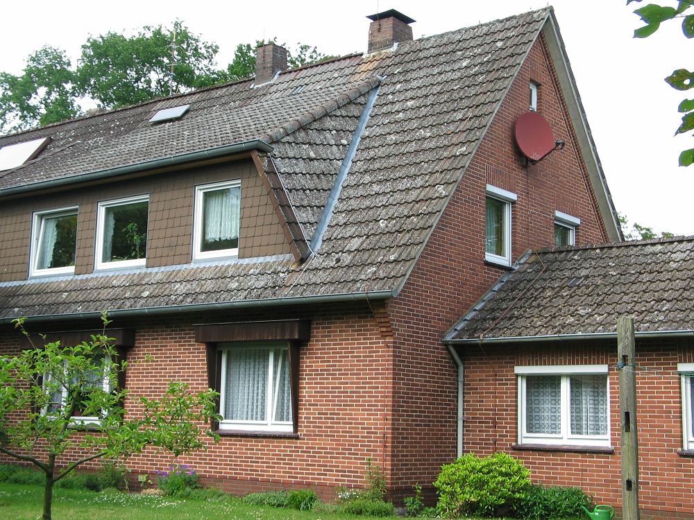 Rotes Backsteinhaus mit grauem Ziegeldach und Satellitenschüssel. Die Fensterrahmen sind weiß.