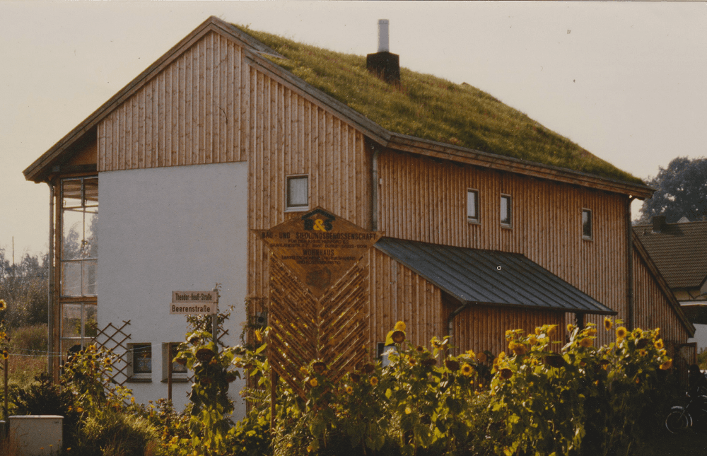 Haus mit Gründach, Holzverkleidung und einem Sonnenblumengarten.