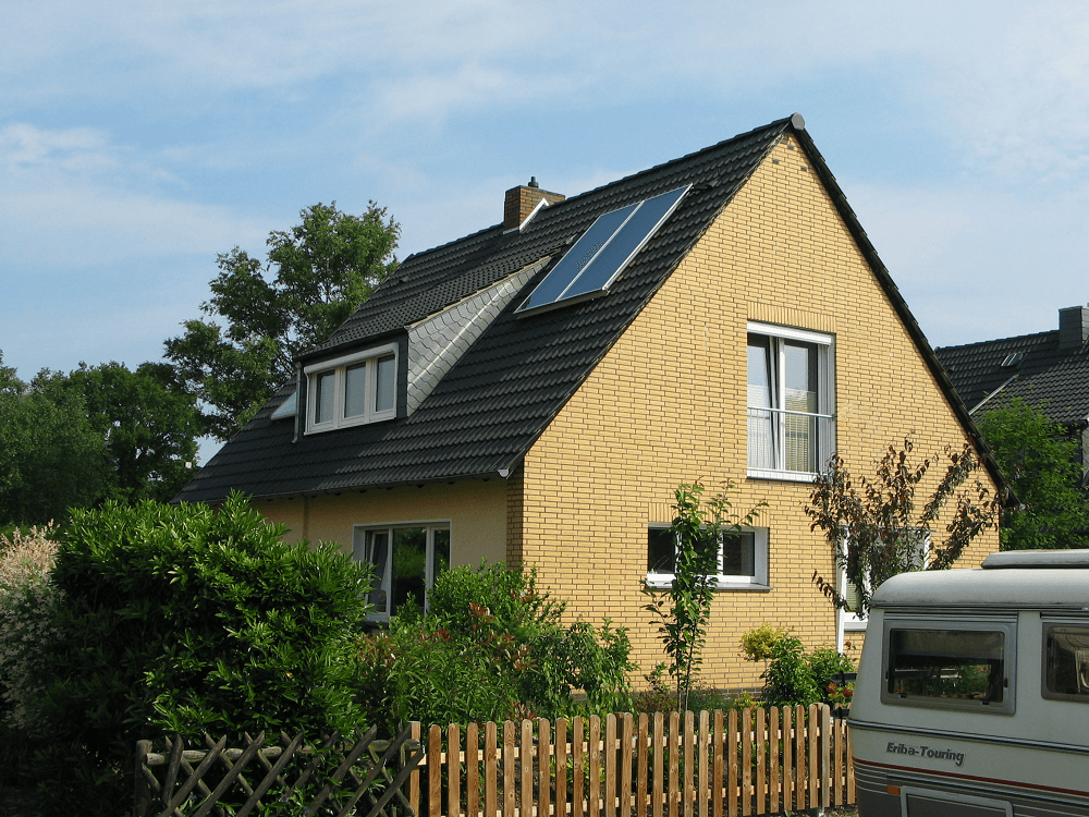 Gelbes Haus mit dunklem Dach, Solarpaneelen, Dachgaube und Holzzaun.
