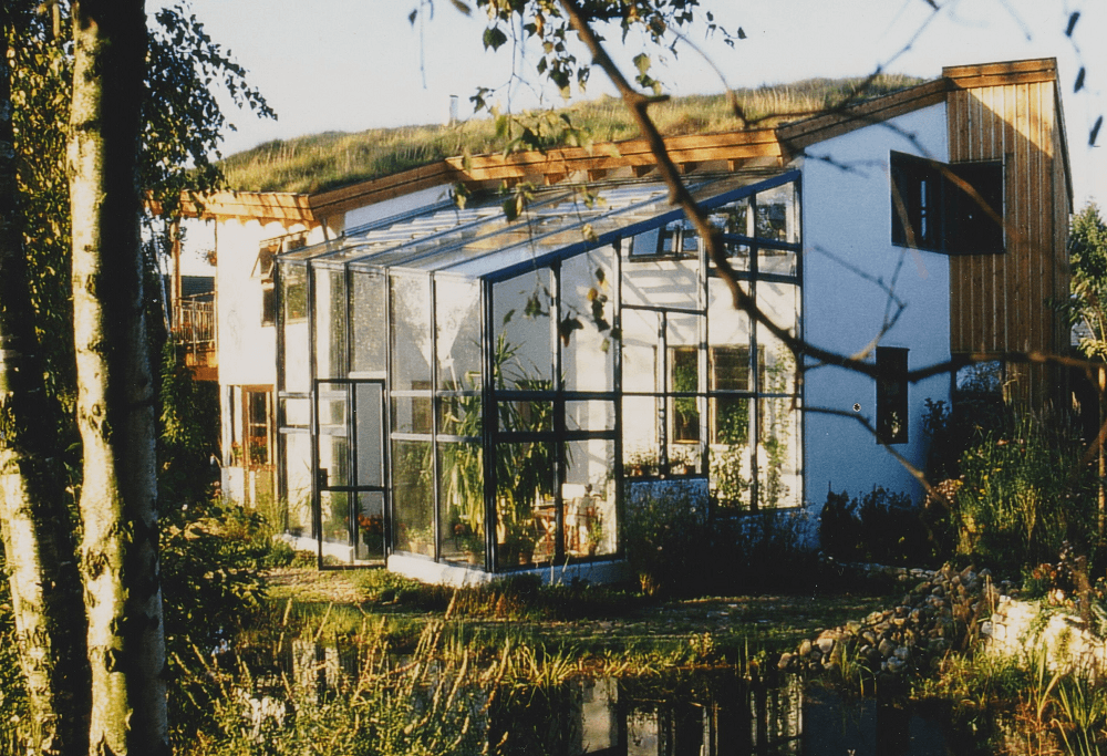 Haus mit Gründach, Gewächshaus und Teich in natürlicher Umgebung.
