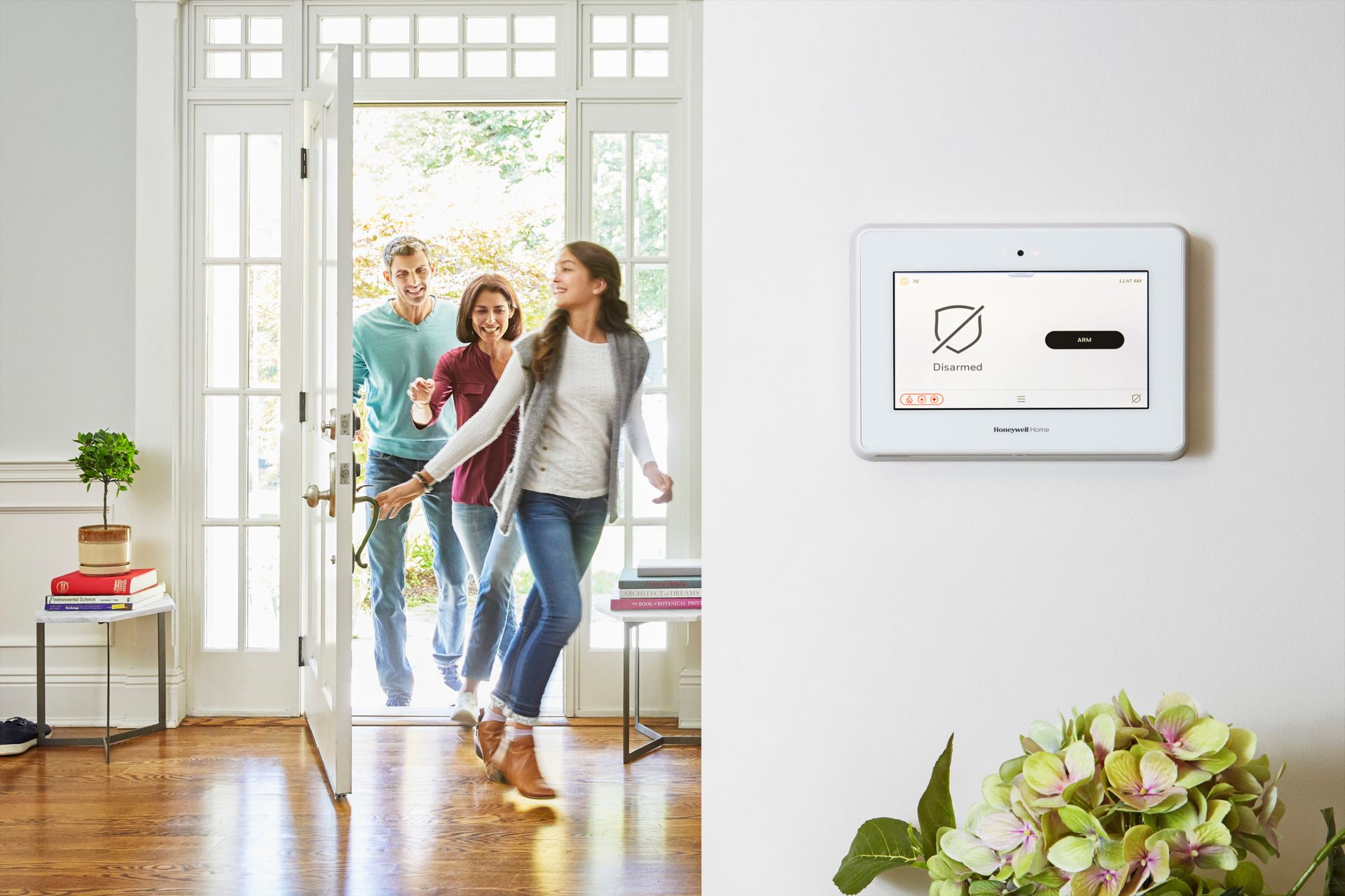 Family entering a home with Resideo security system panel on the wall, door open, and greenery.