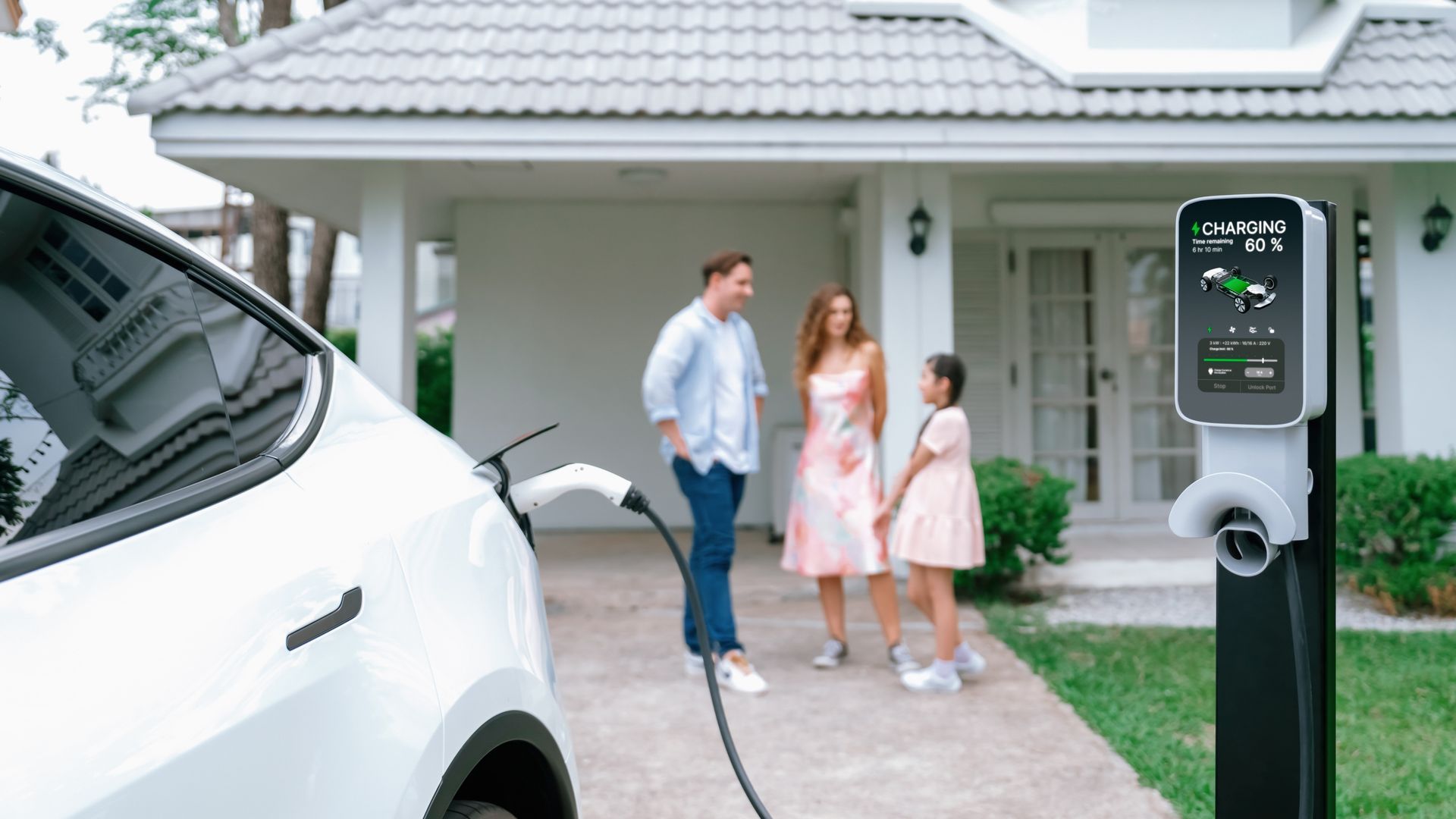 A family is charging their electric car at a charging station in front of their house.