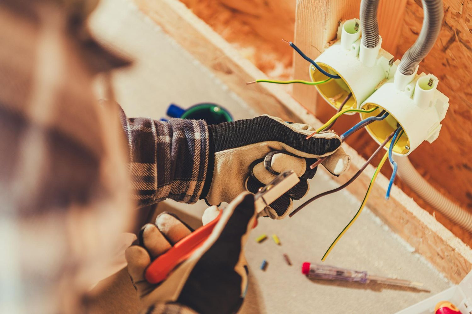 Electrician in gloves wiring electrical outlets, working in a wooden structure.