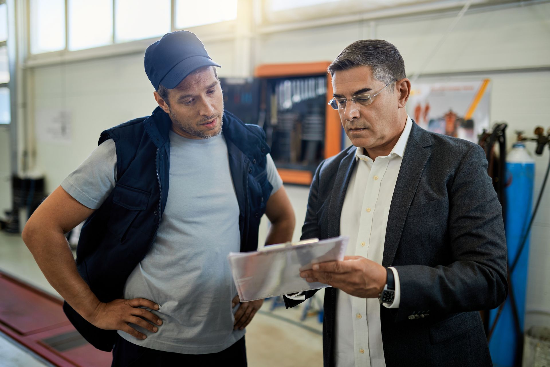 Two men are standing next to each other in a factory looking at a piece of paper.