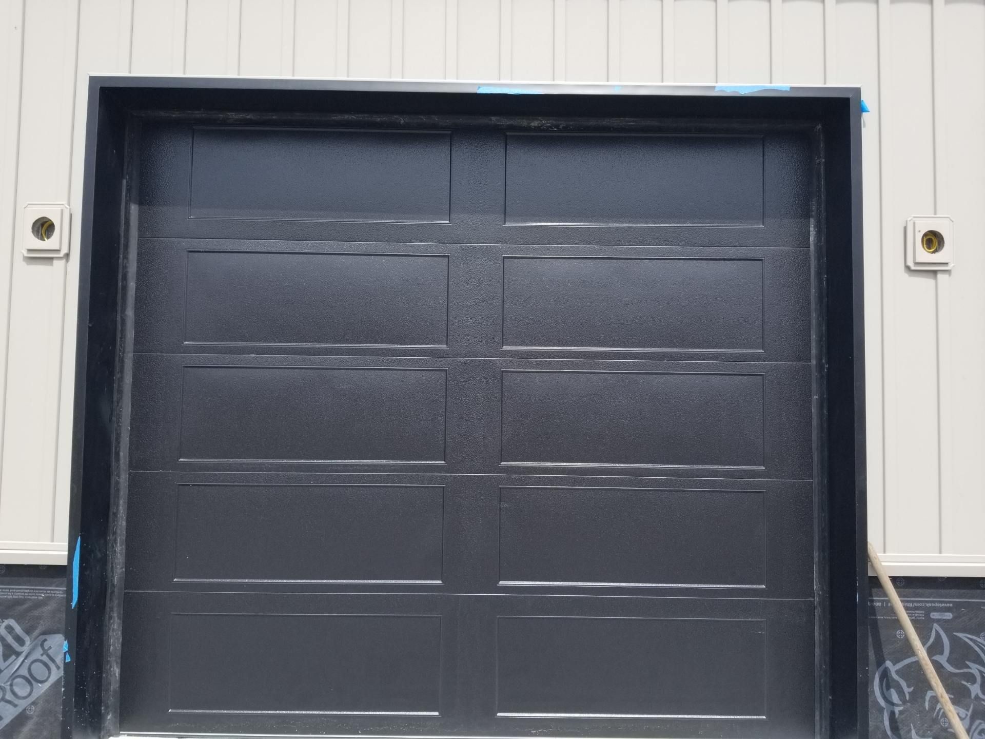 A black garage door is sitting on the side of a building.