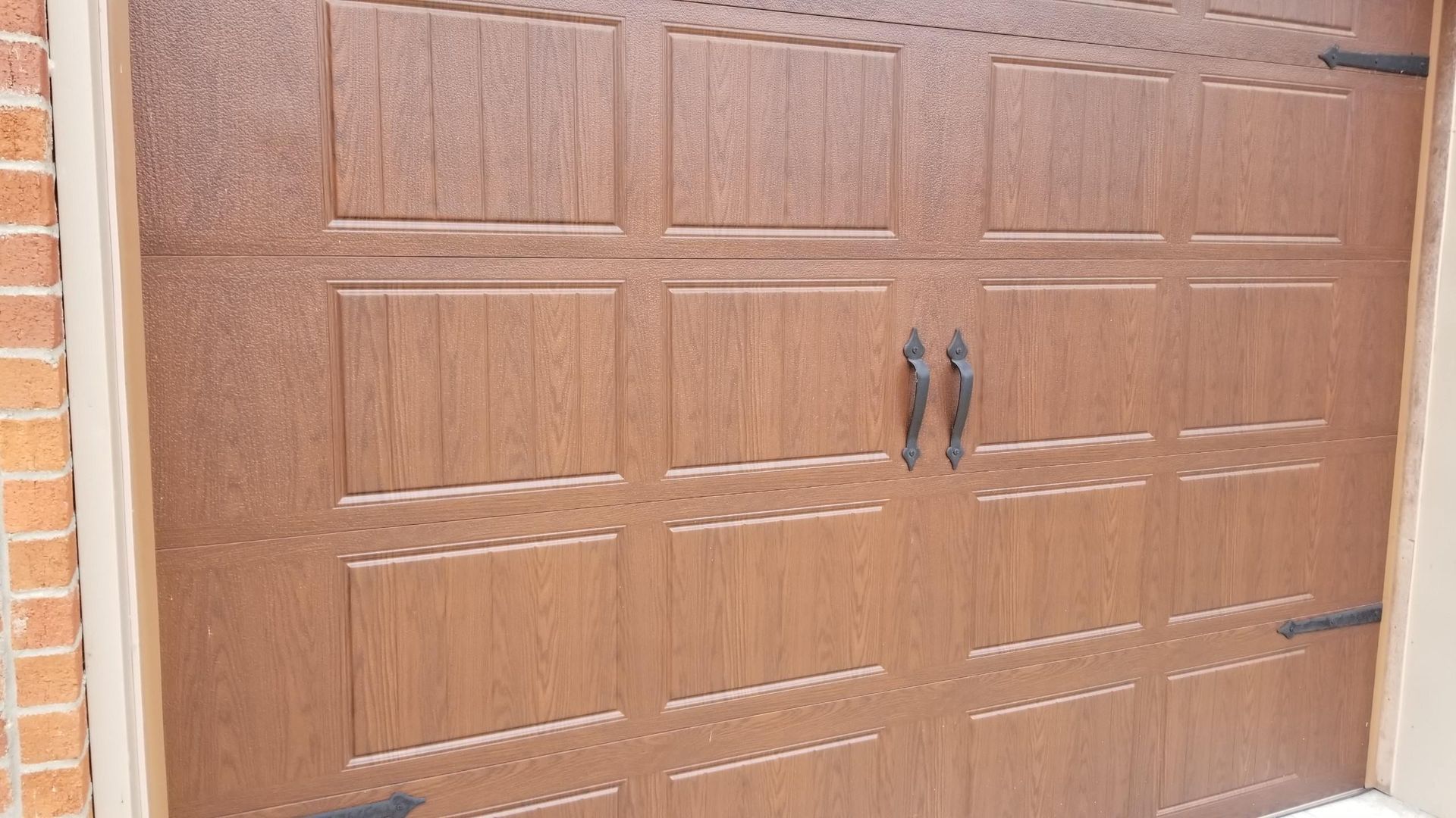 A brown garage door with black handles on a brick wall.