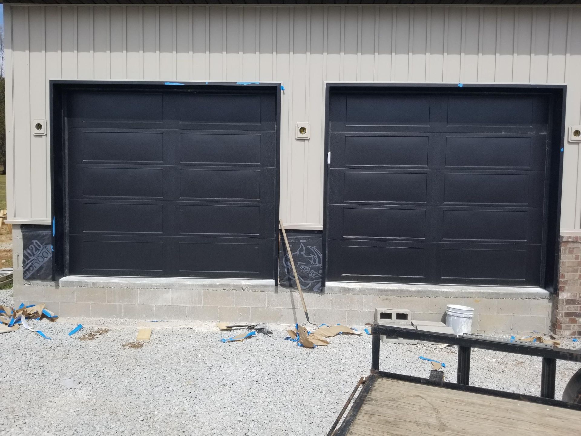Two black garage doors are sitting next to each other on the side of a building.
