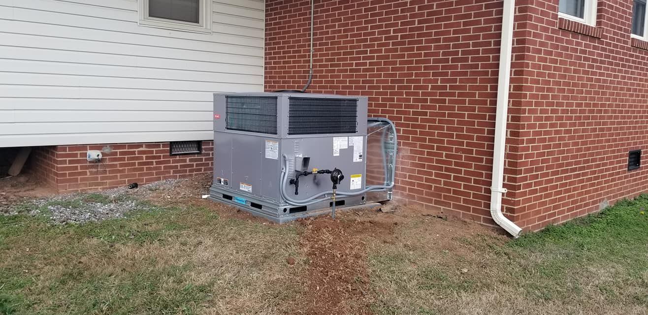 A large air conditioner is sitting on the side of a brick house.