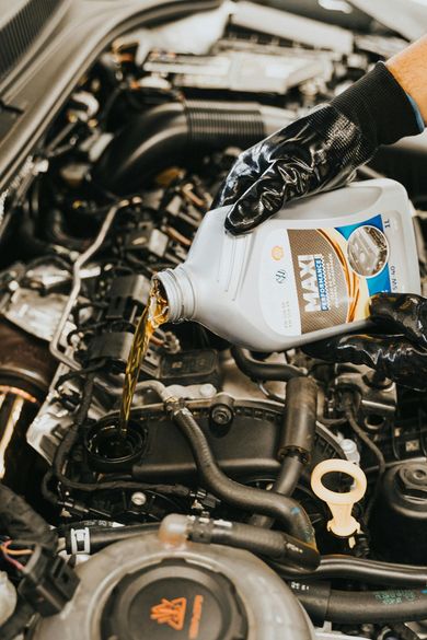 A gloved hand pours golden engine oil from a plastic bottle into an open engine bay.