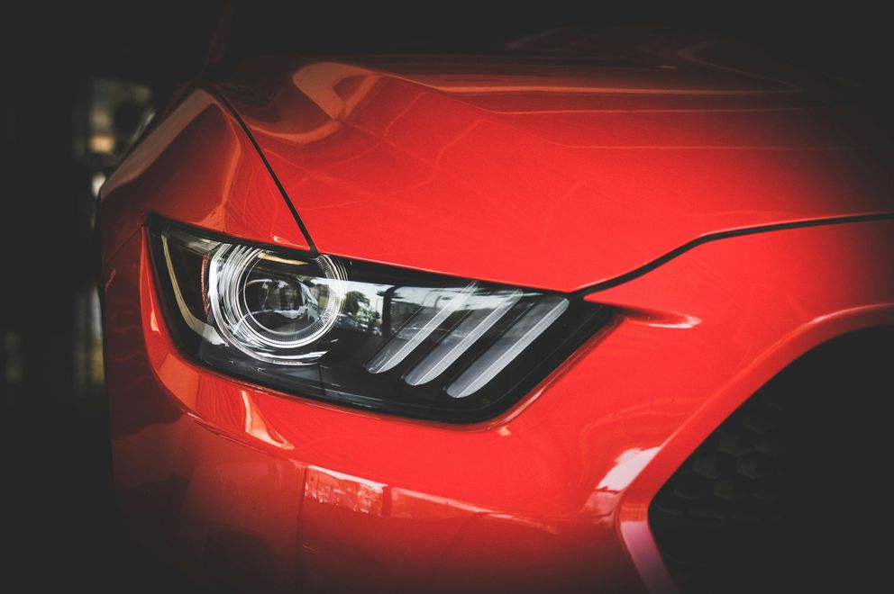 Close-up of a bright red Ford Mustang front headlight with distinctive LED accents.