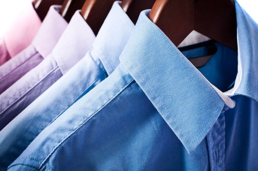 A row of blue shirts hanging on wooden hangers