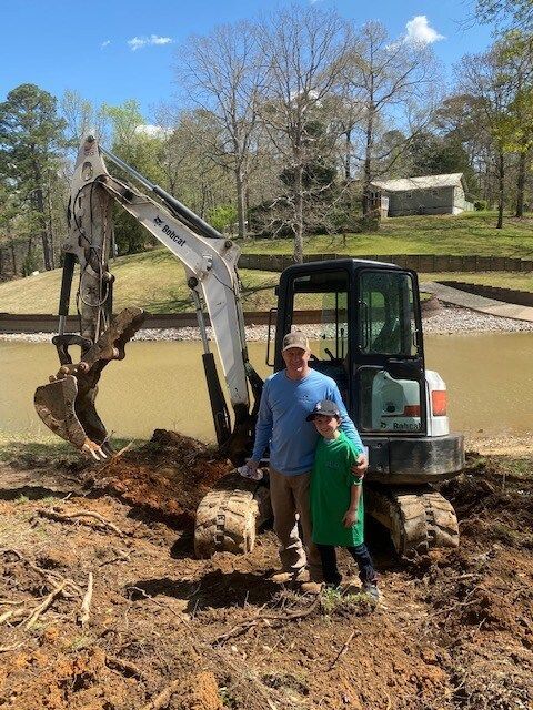 A man and a boy are standing in front of an excavator.