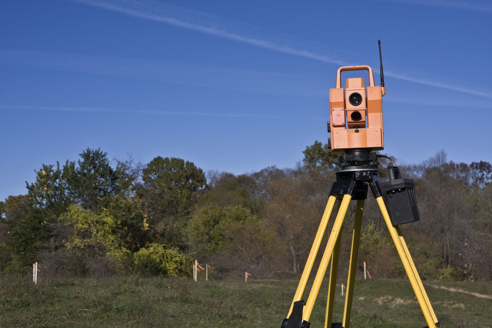 Surveying instrument on tripod in field, measuring land. Bright yellow and orange colors. Blue sky.