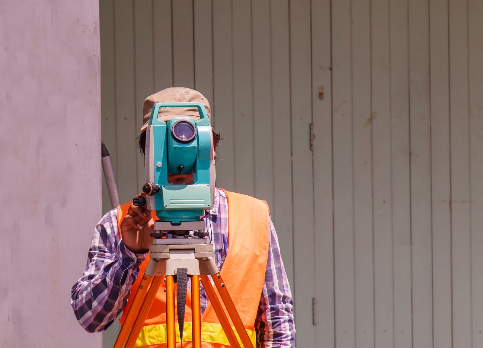 Surveyor using a theodolite, wearing safety vest, outdoors.